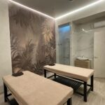 Пример 'элитного ремонта коммерческих помещений': SPA-кабинет с интегрированной душевой зоной, отделанной керамогранитом под мрамор, и акцентной стеной с тропическим панно.