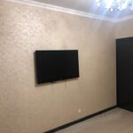 Завершенный 'дизайнерский ремонт квартир': ТВ-зона со стенами, покрытыми декоративной штукатуркой, и темной межкомнатной дверью.