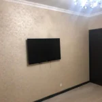 Завершенный 'дизайнерский ремонт квартир': ТВ-зона со стенами, покрытыми декоративной штукатуркой, и темной межкомнатной дверью.